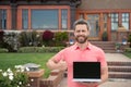 Real estate manager. Happy businessman standing outside near his new home. Suburban house. Young man holding laptop Royalty Free Stock Photo