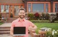 Real estate manager. Happy businessman standing outside near his new home. Suburban house. Young man holding laptop Royalty Free Stock Photo