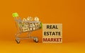 Real estate market symbol. Wooden blocks, words `Real estate market` on beautiful orange background. Shopping cart with miniatur Royalty Free Stock Photo
