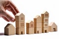 Real estate, rental and investment concept. Human hand placing house shaped wooden blocks together. White background.