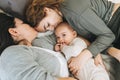 Real family of young mom and two kids of different ages teenager girl and baby boy having fun on the bed