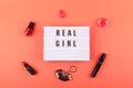 Real girl text on lightbox and decorative cosmetics on coral background. Beauty, makeup flat lay