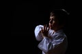 Real karate boy in white kimono isolated on dark background. Child ready for martial arts fight. Kid fighting at judo training.