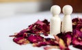 Real love, lover, couple concept. Two wooden figures with red rose petals on white background, standing together