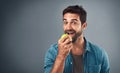 Real men eat real food. Studio shot of a handsome young man eating an apple against a grey background. Royalty Free Stock Photo