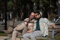 Real marriage of gay couple, holding hands, heads together and eyes closed, sitting on a wooden bench, complicit and happy. Royalty Free Stock Photo