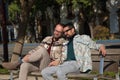 Real marriage of gay couple, holding hands, heads together and eyes closed, sitting on a wooden bench, complicit and happy. Royalty Free Stock Photo