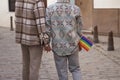 Real marriage of gay couple, holding hands in the street, with a gay pride flag in their pocket and seen from the back. Concept