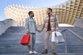 Real marriage of gay couple, holding hands, walking down some stairs and with many shopping bags in the other hand, happy and Royalty Free Stock Photo