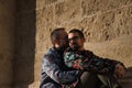 Real marriage of gay couple, sitting on a stone wall while one embraces the other from behind with very affectionate, complicit