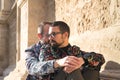 Real marriage of gay couple, sitting on a stone wall while one embraces the other from behind with very affectionate, complicit