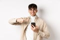 Real people. Handsome young man in glasses pointing finger at smartphone screen, showing online promo, standing on white