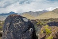 Real petroglyphs on natural stone found in the steppe, on a blurred background of beautiful mountains