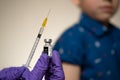 Real Pfizer-BioNTech vaccine vial hold in hand with syringe and child sitting with rolled up sleeve on the blurred background. Edi