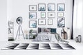 Real photo of a bed standing between a lamp and a chair in a bright bedroom interior with black and white rug and posters on a wa Royalty Free Stock Photo