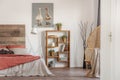 Real photo of a bedroom interior with an oil painting, wooden bookcase and a bed with red and white sheets