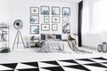 Real photo of a black and white bedroom with a bed standing between a lamp and a chair and next to a wall with plants paintings Royalty Free Stock Photo