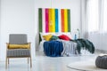 Real photo of a bright bedroom interior with white walls, comfy armchair and colorful blankets on a double bed