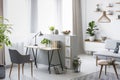 Real photo of a bright home office interior with a desk, armchair and plants