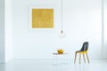 Real photo of a chair standing next to a table with fruit in white simple living room interior with yellow poster Royalty Free Stock Photo