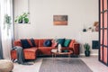 Real photo of colorful pillows on a red corner couch in white living room interior with gray rug Royalty Free Stock Photo