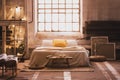 Cozy, industrial bedroom interior with a double bed, yellow pillow, window and chain lights
