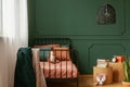 Real photo of a cute, green and orange bedroom interior for a kid with plush fox toys, molding on green wall and books on bedside