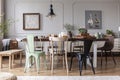 Real photo of an eclectic dining room interior with various chairs at the table, lamp and painting with ducks