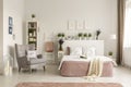 Real photo of a feminine bedroom interior with a comfy armchair, bed, plants and shelf Royalty Free Stock Photo