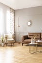 Real photo of full of light daily room with retro armchair, lamp, brown leather couch and tables Royalty Free Stock Photo