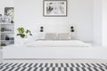 Real photo of a king-size platform bed standing in a white bedroom interior with a patterned rug and shelves in the bacground Royalty Free Stock Photo