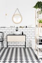 Real photo of a modern bathroom interior with checkered floor, mirror, wash basin with a cupboard and plants