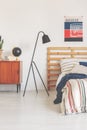 Real photo of a modern lamp in a retro bedroom interior with a bed, poster and wooden cupboard Royalty Free Stock Photo