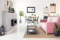 Real photo of open space flat interior with pink velvet sofa, fireplace, dining table and kichenette