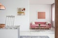 Real photo of paintings in a spacious living room interior with a pink sofa and copper coffee table