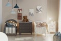 Real photo of a pastel bedroom interior for siblings with wooden cribs, beige walls, and cute teddy bears on a gray chest of Royalty Free Stock Photo