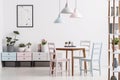 Real photo of a pastel dining room interior with a table, chairs