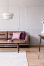 Real photo of pink and purple pillows placed on leather couch in bright living room interior with wainscoting on wall, coffee tabl