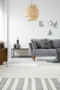 Real photo of a rattan lamp hanging above a gray settee with a b