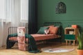 Real photo of a rug shaped like a fox on the wooden floor of a child`s bedroom interior with orange sheets and pillows on a black