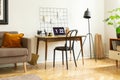 Real photo of a simple desk with a laptop, chair, wall organizer next a sofa in a home office interior
