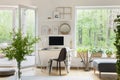 Real photo of white living room interior with big window, glass door, fresh plants, wooden desk with mockup computer and simple po