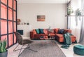 Wicker chair, gray rug and red corner couch in colorful living room interior with green accents Royalty Free Stock Photo