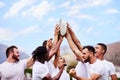 The real prize is comradeship. a group of young rugby players raising a rugby ball in solidarity at a game.