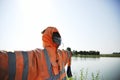 Real scarecrow against a blue sky wearing orange work suit and gloves - Scarecrow with scary face in front of the lake - Halloween