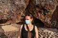 Real young adult girl in a medical mask and sunglasses on her head against the backdrop of cave on Kleopatra beach in Alanya Royalty Free Stock Photo