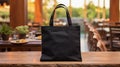 Realistic Black Tote Canvas Fabric Bag Set-up In A Restaurant, Coffee Shop Interior, Tote Mock Up Blank. Black Tote Bag Template