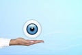 Realistic human eye with blue cornea in the form of a round icon on the palm of a doctor, woman. Gradient blue background. Copy