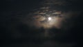 A realtime shot of a full moon on a night sky with visible white clouds.