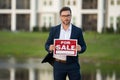 Realtor agent is a realtor with sign for sale in hand against the background on new apartment home background. Realtor